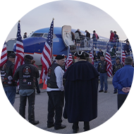 group of people with American flags lined in a row leading to a commercial aircraft